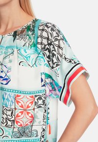 Kurzarmbluse aus buntem, gemustertem Stoff mit einer Mischung aus geometrischen und floralen Designs in Blau, Rot und Schwarz.