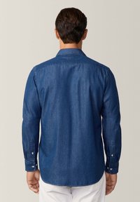 Camicia da uomo in denim a maniche lunghe di colore blu scuro con polsini bottone, colletto a punta e orlo leggermente curvo. Tessuto liscio.