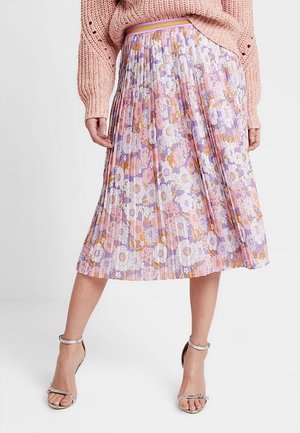 Femme portant une jupe midi plissée à motif floral violet, rose et blanc, associée à un pull rose en maille et des talons argentés à bride cheville.