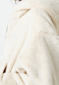Sudadera color crema hecha de un tejido suave y esponjoso, con una textura delicada, hombros caídos y una capucha grande y acogedora.