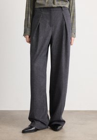 Grau gefaltete weit geschnittene Hosen aus strukturiertem Stoff, mit hoher Taille und kombiniert mit eleganten schwarzen spitzen Schuhen.