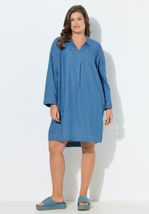 Femme portant une robe ample bleu à rayures fines aux genoux, à manches longues et col, assortie à des sandales plateformes bleues à enfiler.