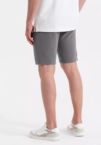Shorts de sport gris avec une taille élastique, texture lisse et poches latérales, associés à des baskets blanches et grises.