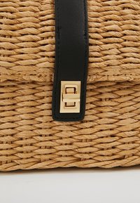 Borsa di paglia intrecciata con una finitura beige testurizzata, dotata di una tracolla in pelle nera e una chiusura rettangolare dorata.