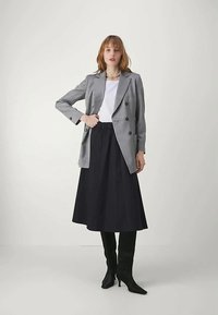 Hallideh halli, millel on valge särk, ja must põlvpüks, täiustatud mustade kõrgete saapatega. Siledad tekstuurid ja viimistletud disain.