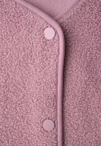 Lähikuva vaaleanpunaisesta, teksturoidusta kankaasta, jossa on kiharat kuidut, siistit reunat ja kaksi sopivaa pyöreää nepparipainiketta.