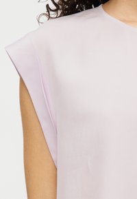 Ροζ ανοιχτόχρωμο τοπ με κοντά μανίκια, που διαθέτει ομαλή υφή και άνετη εφαρμογή, με διακριτική λεπτομέρεια σε ραφές στα μανίκια.