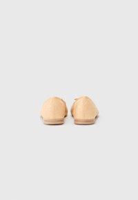 Mocassins beiges en tissu texturé avec un motif subtil, présentant une semelle lisse et un bout arrondi. Aucun détail de quincaillerie visible.