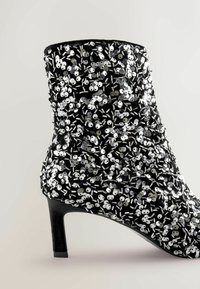 Mustad mustatsi saabaste peal on peegeldavad sädelused, mis on kaunistatud tsükliliste detailidega. Kingal on mõõdukalt kõrge konts ja ümar nina.