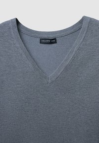 Maglione grigio a scollo a V realizzato in morbido tessuto a maglia. Presenta un collo a coste piatte e un'etichetta "CALLIOPE XS/S". Design minimalista con una trama uniforme.