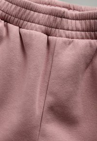 Lichtroze joggingbroek met een gerimpelde elastische tailleband en een gladde, zachte stof met subtiele textuur zonder zichtbare patronen of accenten.