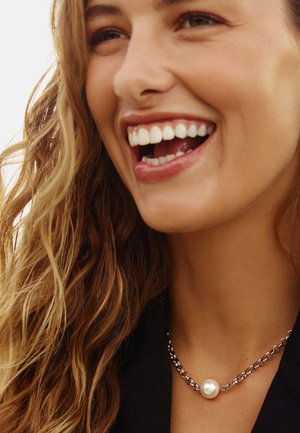 Collar de cadena de plata con un único colgante de gran perla, que muestra una superficie lisa y un acabado lustroso sobre un fondo de tela oscura.