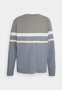 Maglietta a maniche lunghe con girocollo, caratterizzata da strisce orizzontali grigie, bianche, blu e taupe, e una tasca sul petto lato sinistro.