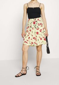 Černý top na tenkých ramínkách s žlutou květinovou sukní s červenými růžemi, nařaseným pasem a černou kabelkou. Styl dokončují černé sandály na podpatku.