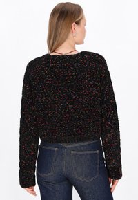 Maglione nero a maglia con macchie colorate, caratterizzato da un design cropped e maniche lunghe. Il tessuto testurizzato aumenta l'interesse visivo.