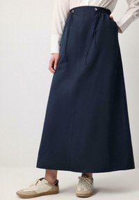 Long navy skirt with drawstring waist, made of smooth fabric. Paired with light-colored sneakers featuring a mix of materials.