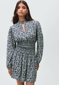 Kvetinové šaty v tmavošedej farbe s svetlo modrými vzormi. Obsahujú smockovaný pás, dlhé nafúknuté rukávy a detail výstrihu v tvare kľúčovej dierky.