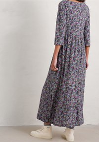 Maksikjole med blomsterprint i mørke farver, med plisseret design, trekvartærmer og slidser i siden; båret med cremede sneakers.