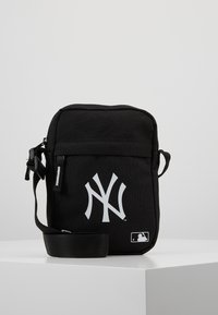Borsa a tracolla nera realizzata in tessuto resistente, presenta un grande logo bianco dei New York Yankees e un'etichetta MLB, con chiusura con zip e tracolla regolabile.