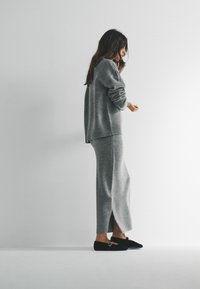 Szary dzianinowy sweter i pasująca spódnica, miękka tekstura, luźny krój, rozcięcie po boku spódnicy. Obuwie: czarne wsuwane buty z klamrą.