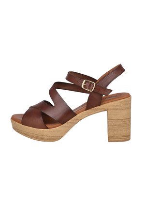 Sandalia de cuero marrón con punta abierta, tiras cruzadas, hebilla en el tobillo y tacón bloque de madera clara.