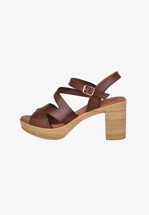 Sandalia de cuero marrón con punta abierta, tiras cruzadas, hebilla en el tobillo y tacón bloque de madera clara.