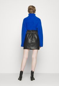 Modrá pletená sveter s vysokým golierom, skombinovaný s čiernou koženou mini sukňou. Čierne členkové topánky dopĺňajú outfit.