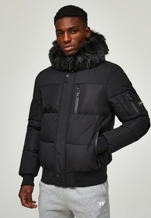Schwarze gepolsterte Jacke mit einem Kragen aus Kunstfell, ausgestattet mit Reißverschlusstaschen und Druckknöpfen. Das Material ist glatt und hat eine matte Oberfläche.