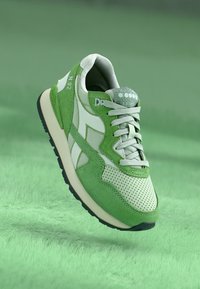 Green athletic sneaker featuring a mix of textured mesh and suede, with perforations, white accents, and a black rubber sole.