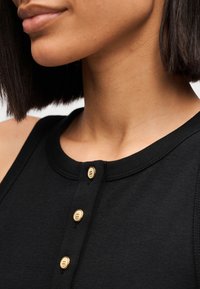 Μαύρο τοπ χωρίς μανίκια με στρογγυλή λαιμόκοψη, διακοσμημένο με τρία χρυσά κουμπιά μπροστά και ριμπ υφή κατά μήκος της λαιμόκοψης και των μασχαλών.