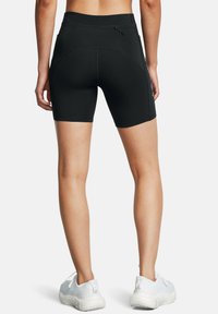 Pantaloni corti sportivi neri con design aderente, lunghezza a metà coscia, texture liscia e una tasca con zip sul retro.