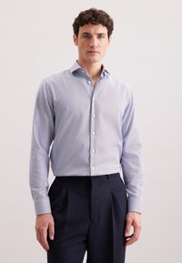 Camicia abbottonata in azzurro chiaro con un piccolo motivo a quadretti, maniche lunghe e colletto. Abbinata a pantaloni scuri in navy.