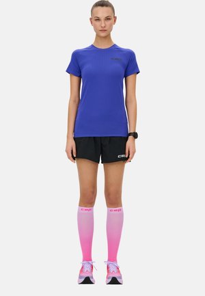 Sportoutfit mit einem blauen Kurzarmshirt, schwarzen Shorts und knielangen, pinkfarbenen Socken mit Farbverlauf. Enthält Schuhe mit pinken Akzenten.