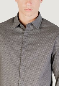 Primo piano di un uomo che indossa una camicia grigia a bottoni con un piccolo motivo geometrico e colletto a punta.