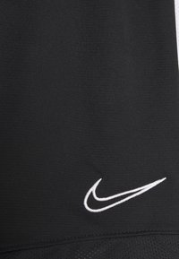 Svart sporttröja med strukturerad tyg och en vit broderad Nike-swoosh-logotyp nära fållen.