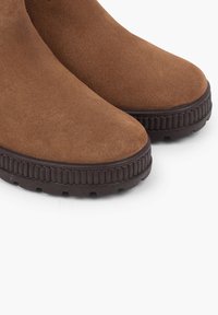 Bocanci din suede maro până la gleznă, cu vârful rotund și o talpă groasă din cauciuc maro închis, dotată cu striații orizontale pentru aderență.
