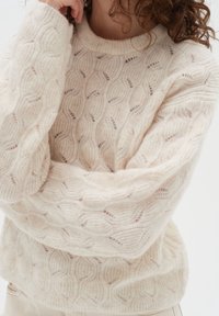 Ljuscremegarntröja med en texturerad vågmönster, rund halsringning och avslappnad passform med sänkta axelsömmar.