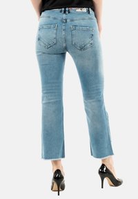 Jeans svasati azzurro chiaro con orlo grezzo, dotati di tasche posteriori e vita medio-alta, abbinati a tacchi alti neri.