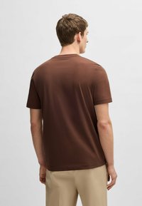 T-shirt corto marrone a maniche corte realizzato in tessuto morbido, con colletto a girocollo. Il design è a vestibilità comoda senza motivi o dettagli visibili.