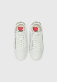 Ténis brancos de couro com uma faixa prateada, design com atacadores e palmilha estampada com um coração vermelho e o texto "LOVE MOSCHINO".
