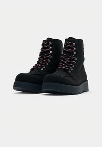 Botas de senderismo negras con cordones de patrón rojo y azul, suelas de goma resistentes y una parte superior texturizada, que presenta ojales de metal y un diseño de caña alta.