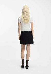 Top bianco a maniche corte a coste abbinato a una gonna nera. Presenta un design aderente e una finitura testurizzata. Scarpe nere con suole spesse e calzini trasparenti.