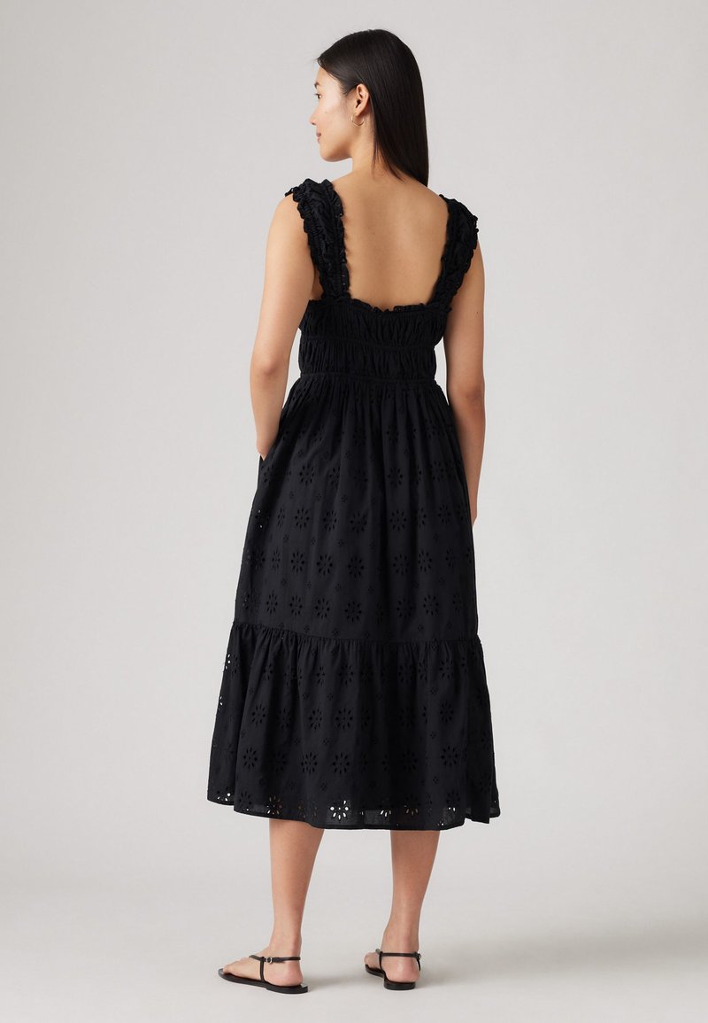Vestido negro sin mangas con tirantes con volantes, que presenta un cuerpo fruncido y una falda de capas con patrones florales bordados.