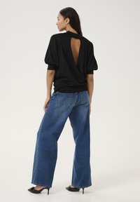 Un haut en tricot noir avec une grande découpe dans le dos, associé à un jean oversized bleu taille haute. Des escarpins à talons aiguilles complètent la tenue.