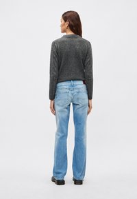 Jersey gris con textura, vaqueros azul claro de pierna recta, zapatos negros gruesos. El conjunto presenta un ajuste relajado y detalles de costuras visibles.