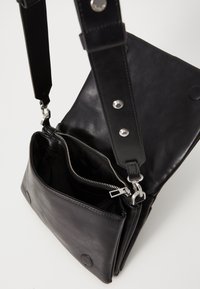 Borsa a spalla in pelle nera con finitura testurizzata, dotata di dettagli in metallo argentato, un comparto con zip e tracolla regolabile.