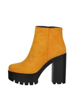 Botas de ante amarillas hasta el tobillo con una plataforma negra gruesa y un tacón alto de bloque, que cuentan con una textura suave y un diseño de punta redondeada.