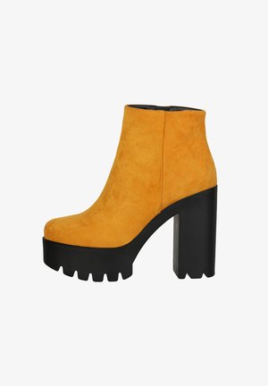 Botas de ante amarillas hasta el tobillo con una plataforma negra gruesa y un tacón alto de bloque, que cuentan con una textura suave y un diseño de punta redondeada.