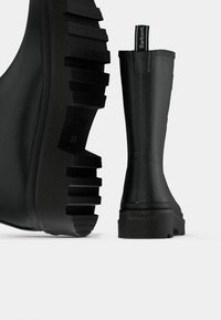 Μαύρα λαστιχένια μποτάκια αστραγάλου με χοντρή, υφή σόλα διαθέτουν ανάγλυφο λογότυπο της μάρκας στη φτέρνα και θηλιά για εύκολη εφαρμογή.