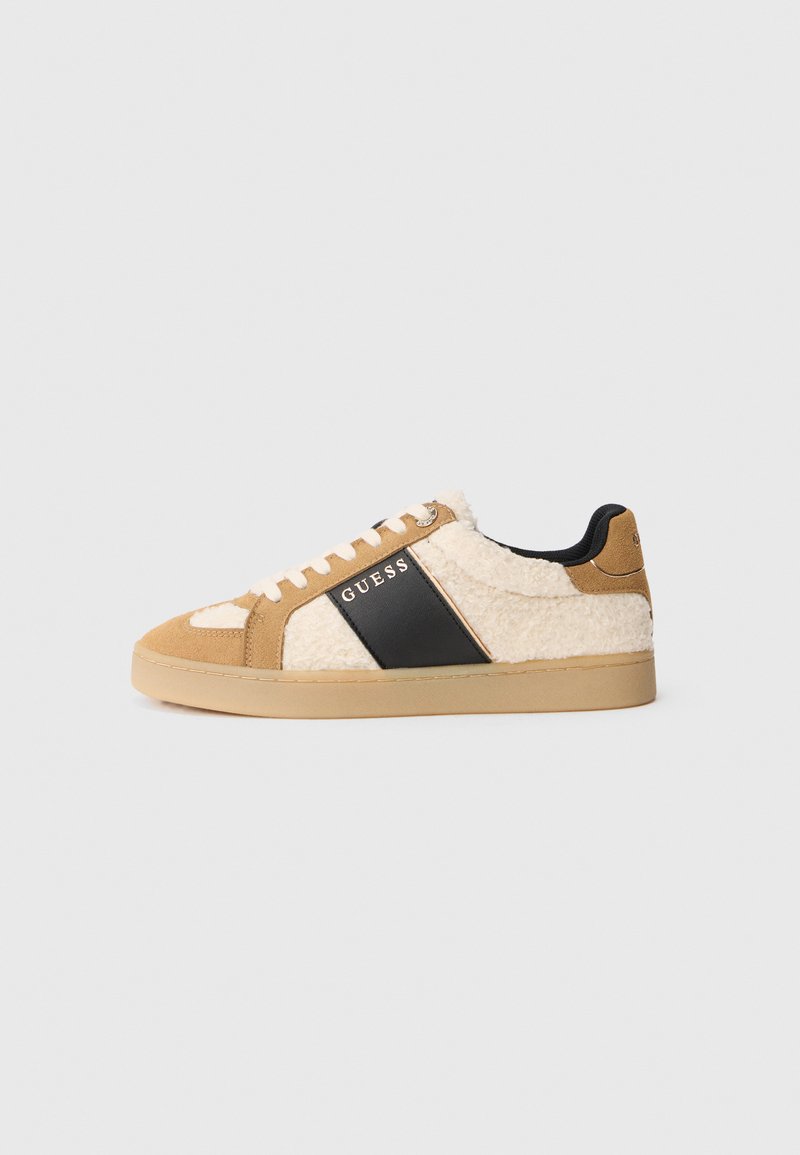 Sneakers beige e crema con una tomaia morbida simile alla pelliccia, striscia laterale nera, lacci bianchi e suola in gomma. Il nome del brand "GUESS" è visibile.